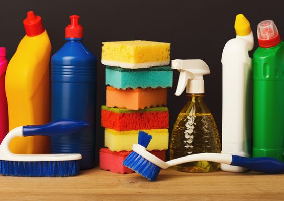 Group of colorful cleaning products on dark background. Different bottles, sponges, brushes and mop on wood table. House keeping, tidying up, spring-cleaning concept, copy space